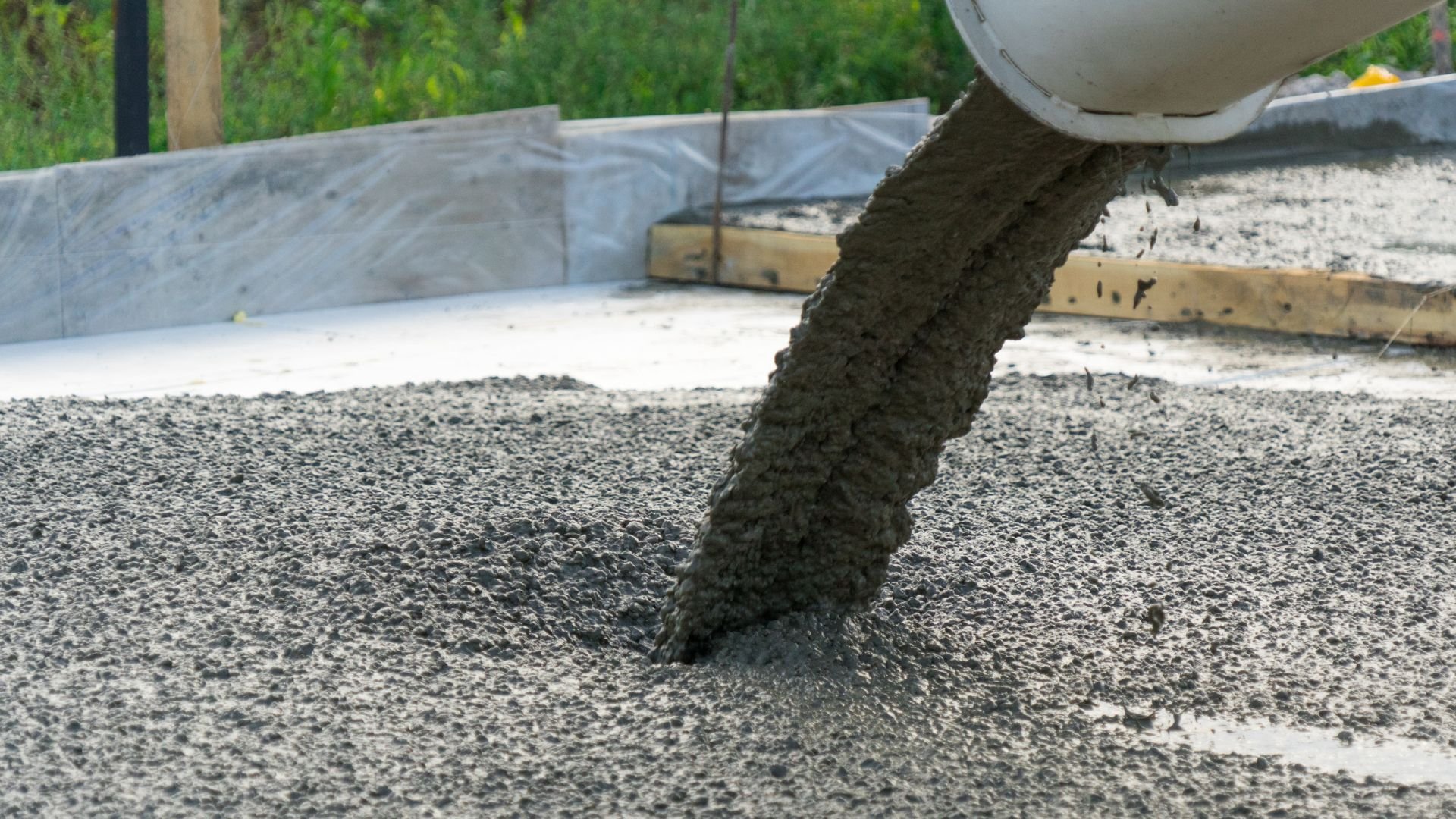 Wet concrete pouring from mixer chute onto construction site ground